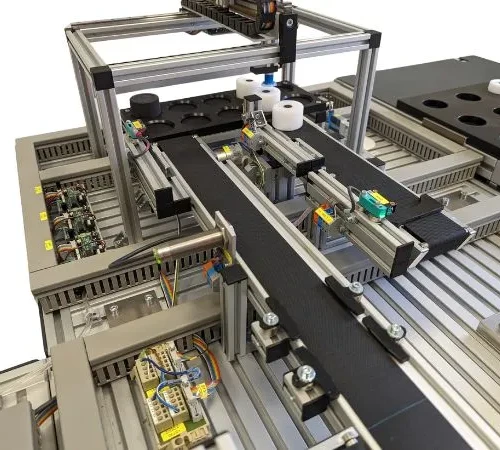 Fragment stacji dydaktycznej intralogistyki – magazyn powierzchniowy z robotem kartezjańskim i systemem transportowym, w tle stanowisko paletyzacji cobota. Zdjęcie magazynu powierzchniowego z robotem kartezjańskim i systemem transportowym, w tle stanowisko paletyzacji cobota