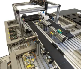 Fragment stacji dydaktycznej intralogistyki – magazyn powierzchniowy z robotem kartezjańskim i systemem transportowym, w tle stanowisko paletyzacji cobota.